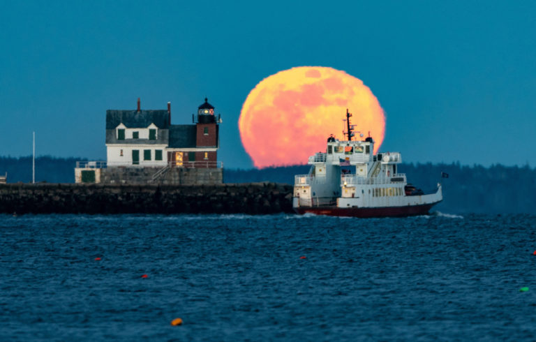 A Maine State Ferry Service boat rounds the Rockland Breakwater as a full moon rises.