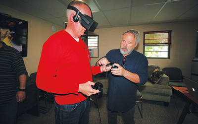 Chuck Carter, founder of Eagre Games and developer of a recently debuted game called ZED, helps First National Bank CEO Tony McKim don VR goggles and controllers.