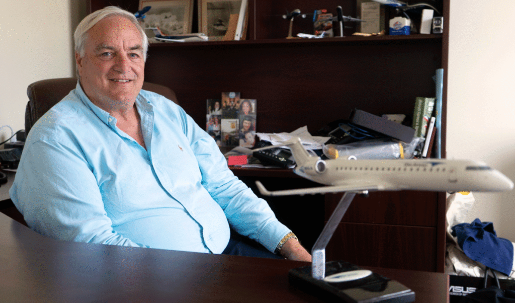 John Pearsall poses in the Portland offices of Elite Airways with a model of one of the aircraft his company flies.