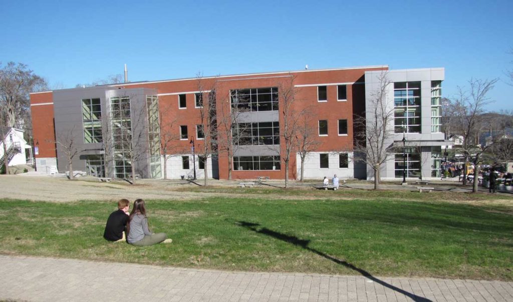 Two young adults sit on the grass in front of Maine Maritime Academy's new ABS Center during the dedication ceremony.