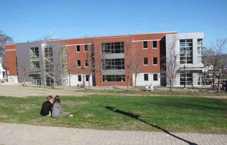 Two young adults sit on the grass in front of Maine Maritime Academy's new ABS Center during the dedication ceremony.