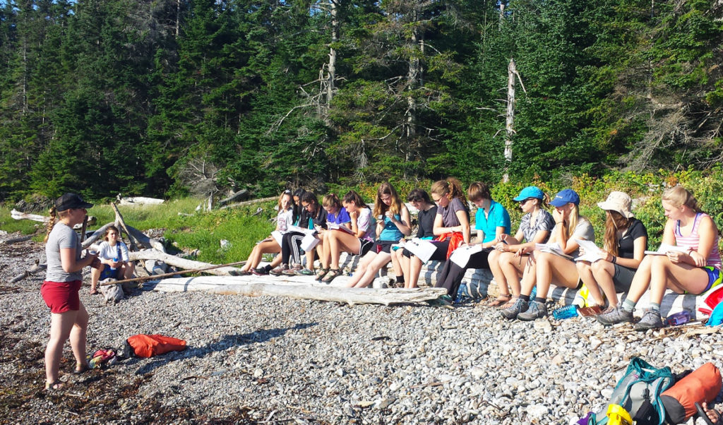 Students sit on the shore during a lesson.