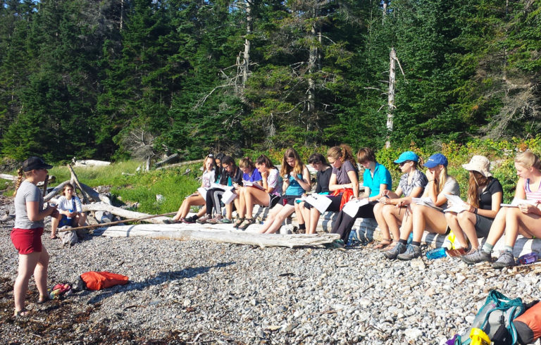 Students sit on the shore during a lesson.