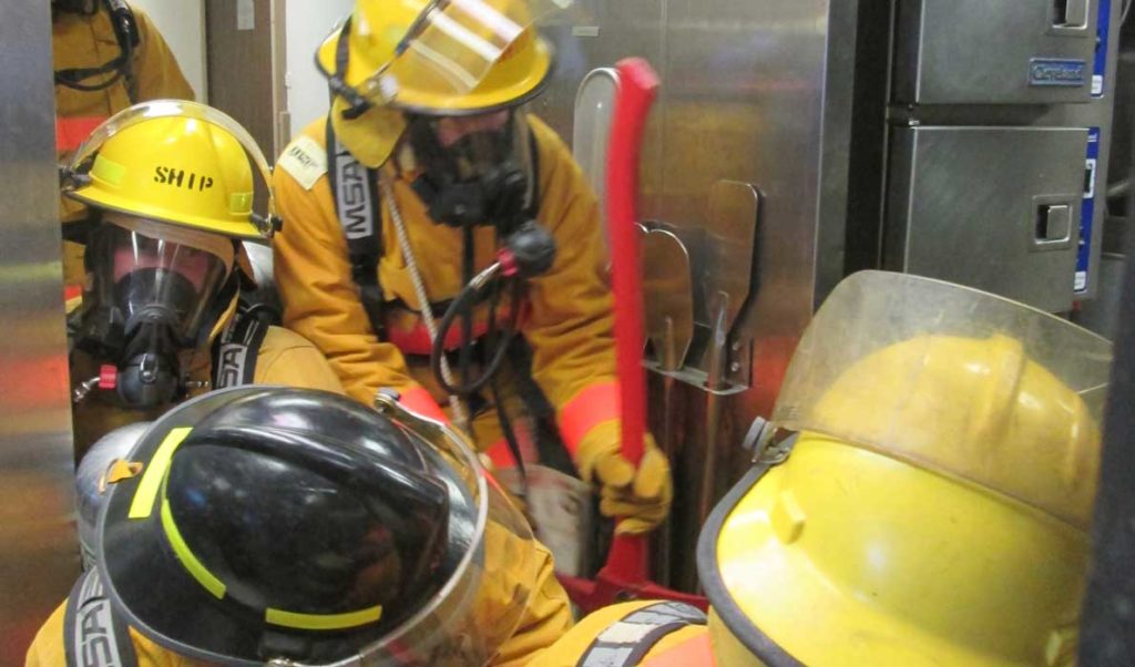 Firefighters squeeze into the galley to fight a simulated grease fire.