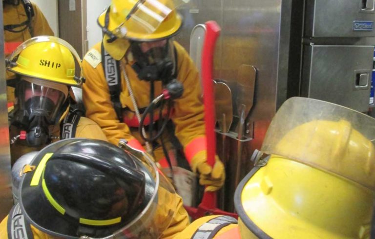 Firefighters squeeze into the galley to fight a simulated grease fire.