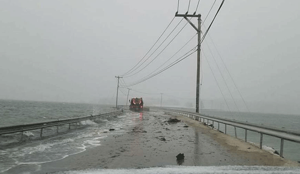 A windshield view of the causeway during a storm, with waves lapping over the pavement.