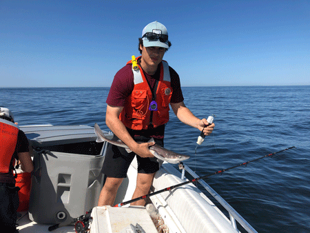 UNE student Ben Gowell holds a dogfish in one hand and a bycatch reduction device in the other.