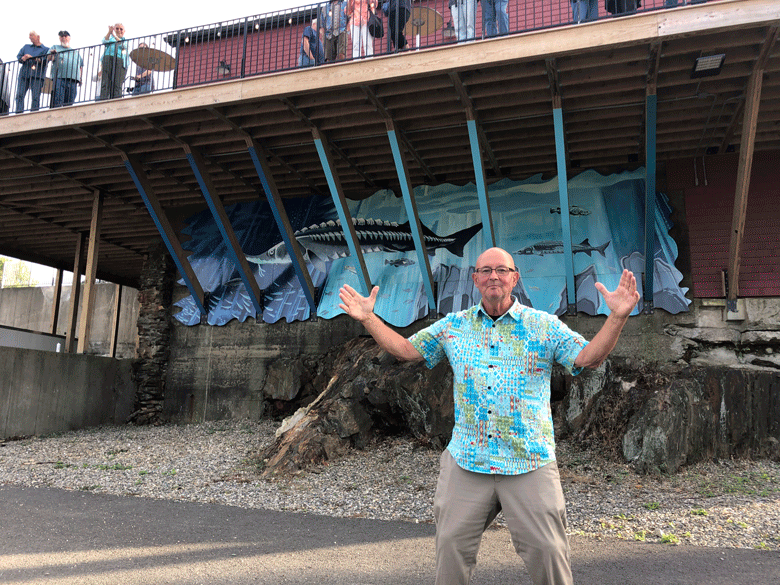 Artist David Hurley poses near his sturgeon mural on the Bayview Events Center, near Belfast’s harbor walk. PHOTO: TOM GROENING